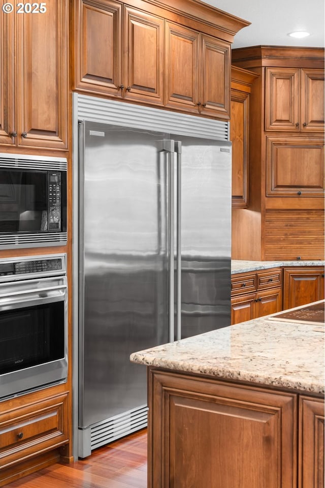 kitchen featuring light wood-type flooring, light stone counters, and built in appliances