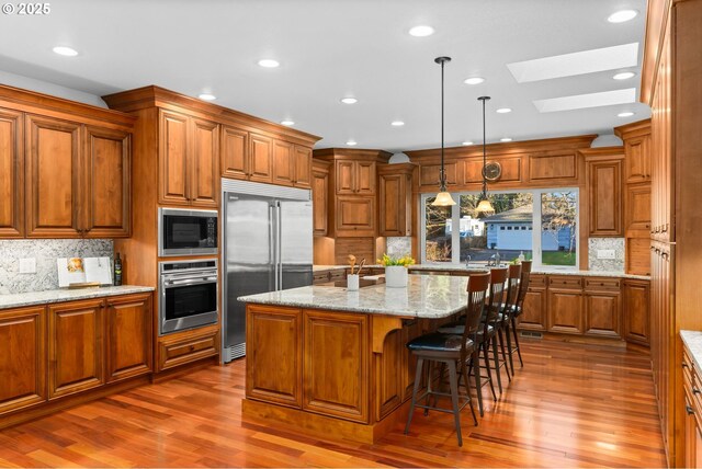 kitchen featuring black electric stovetop, a skylight, sink, hanging light fixtures, and light stone counters