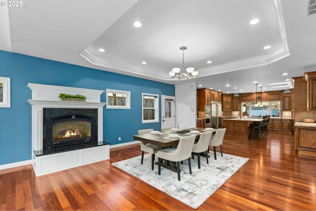 dining room featuring dark wood-type flooring, a high end fireplace, a raised ceiling, and an inviting chandelier