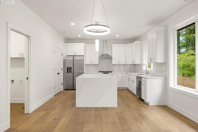 8120 SE 145th Ct, Portland, OR 97236 - kitchen featuring appliances with stainless steel finishes, wall chimney exhaust hood, a center island, light wood finished floors, and decorative backsplash