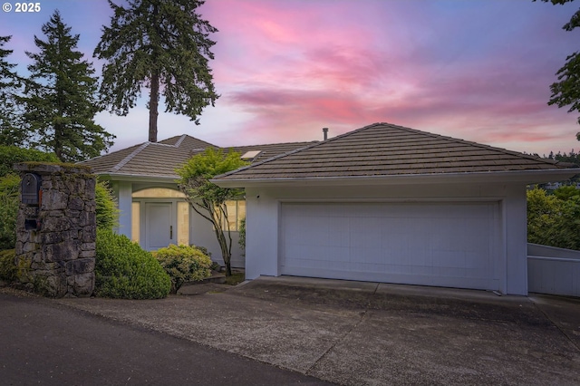 ranch-style home featuring a tile roof, stucco siding, driveway, and an attached garage