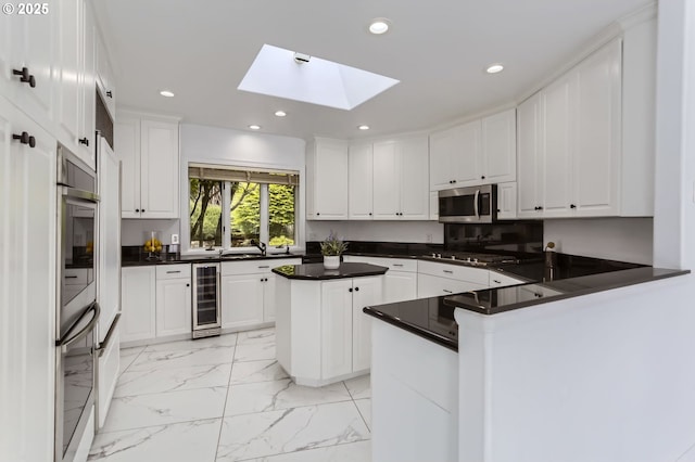 kitchen with beverage cooler, stainless steel microwave, a skylight, recessed lighting, and a peninsula