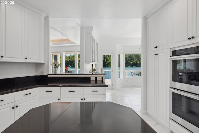 1308 Northshore Rd, Lake Oswego, OR 97034 - kitchen with stainless steel double oven, dark countertops, light marble finish floors, white cabinets, and healthy amount of natural light
