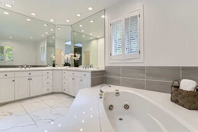 bathroom featuring marble finish floors, a tub with jets, double vanity, and recessed lighting
