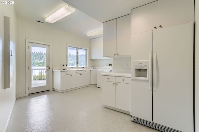kitchen featuring white refrigerator with ice dispenser, washer / dryer, light countertops, and white cabinetry