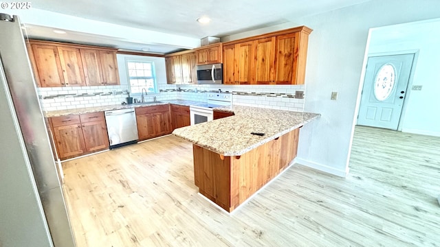 kitchen featuring tasteful backsplash, a sink, light wood-style floors, a peninsula, and appliances with stainless steel finishes