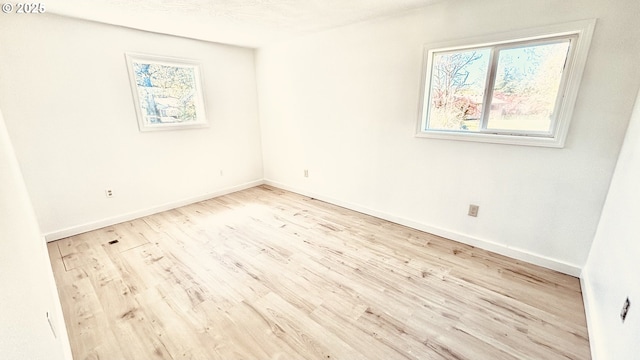 spare room with baseboards, wood finished floors, and a healthy amount of sunlight