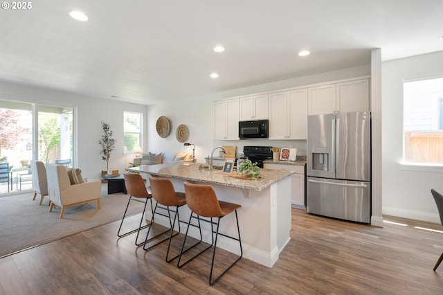 2310 S Heather St, Cornelius, OR 97113 - kitchen with black appliances, recessed lighting, wood finished floors, a kitchen breakfast bar, and white cabinetry