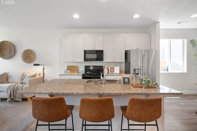 2310 S Heather St, Cornelius, OR 97113 - kitchen with black appliances, a kitchen bar, recessed lighting, light stone countertops, and a center island with sink