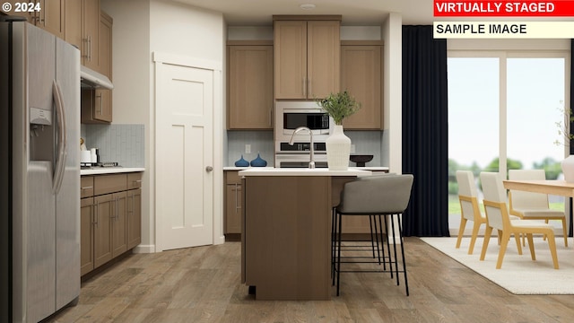 kitchen with a kitchen bar, decorative backsplash, light hardwood / wood-style flooring, and appliances with stainless steel finishes