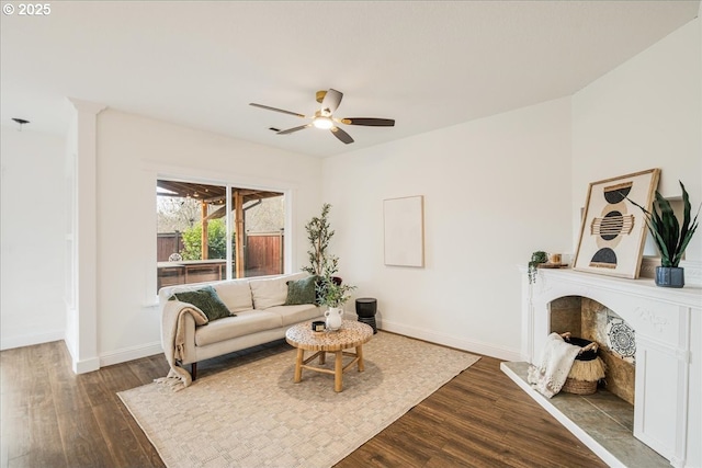 living area with a fireplace with raised hearth, wood finished floors, a ceiling fan, and baseboards