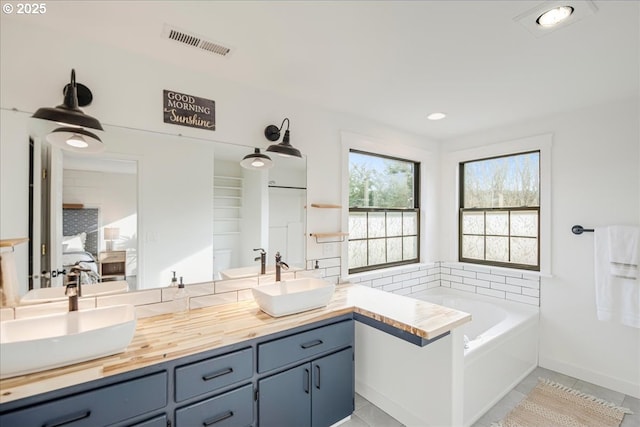 full bath with double vanity, visible vents, a sink, and a bath