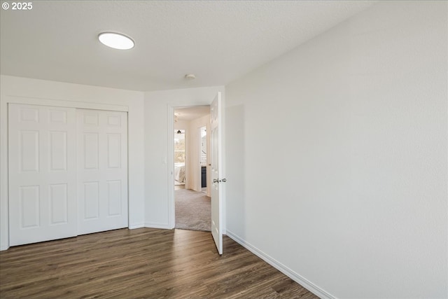 unfurnished bedroom with a textured ceiling, a closet, dark wood finished floors, and baseboards