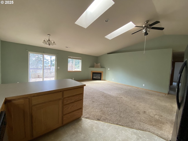 unfurnished living room featuring light carpet, vaulted ceiling with skylight, visible vents, a glass covered fireplace, and ceiling fan