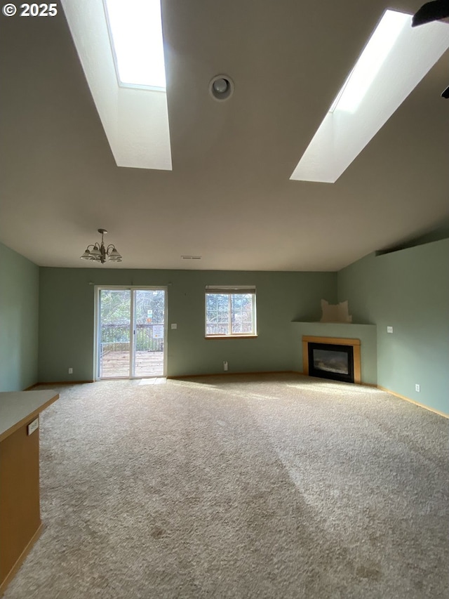 unfurnished living room with carpet floors, a glass covered fireplace, and vaulted ceiling with skylight