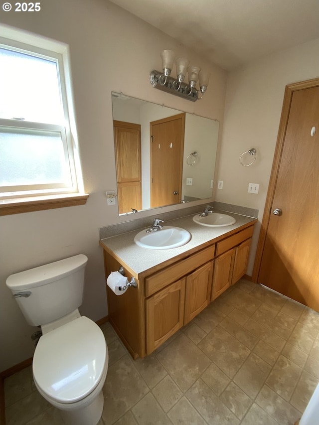 bathroom with toilet, double vanity, and a sink