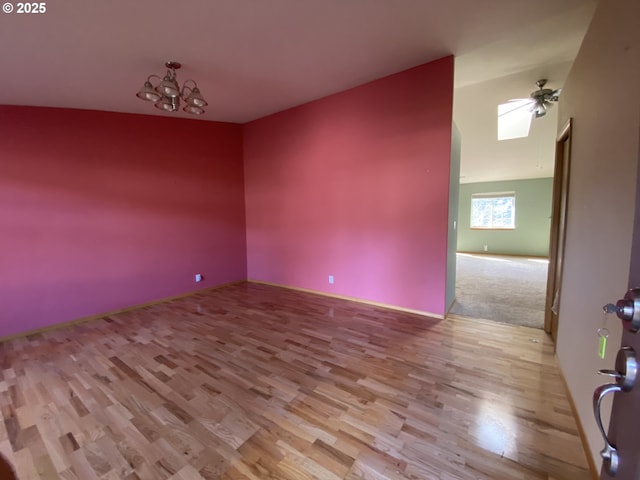 spare room featuring wood finished floors and ceiling fan with notable chandelier