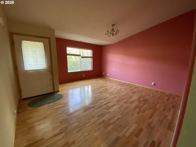 empty room with lofted ceiling, light wood finished floors, and a notable chandelier