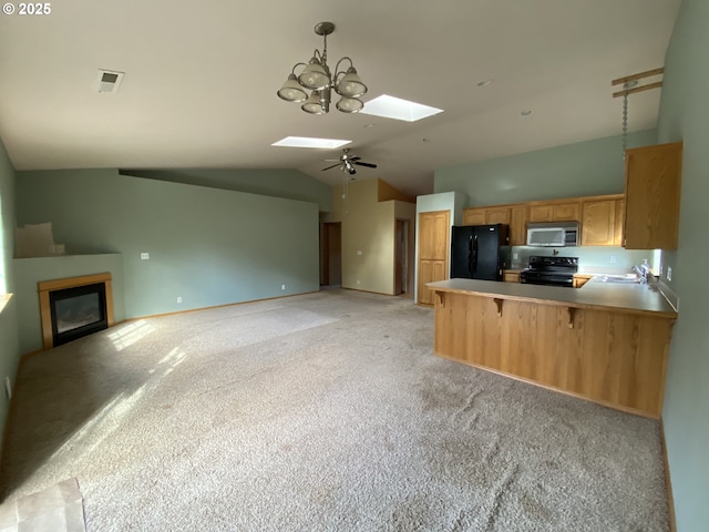 kitchen featuring vaulted ceiling with skylight, a peninsula, a sink, black appliances, and a glass covered fireplace