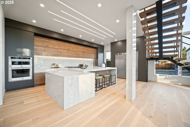 kitchen with a large island, modern cabinets, stainless steel appliances, light wood-style floors, and backsplash