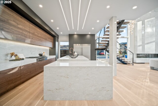 kitchen with modern cabinets, appliances with stainless steel finishes, light stone countertops, light wood-type flooring, and a large island with sink