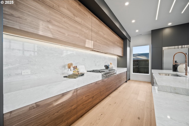 kitchen with modern cabinets, light stone counters, light wood-style floors, a sink, and built in fridge