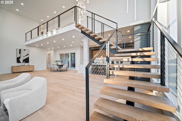 stairs with recessed lighting, a notable chandelier, wood finished floors, a towering ceiling, and baseboards