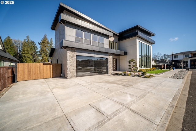 contemporary house featuring driveway, stone siding, an attached garage, and fence