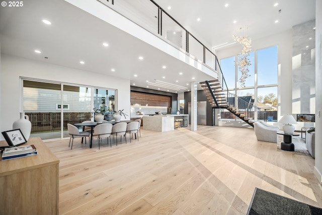 interior space featuring light wood finished floors, a towering ceiling, stairs, a notable chandelier, and recessed lighting