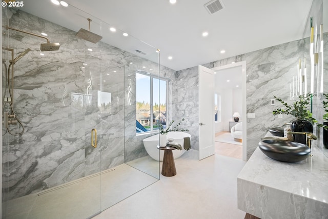 bathroom with a marble finish shower, visible vents, a soaking tub, a sink, and tile walls