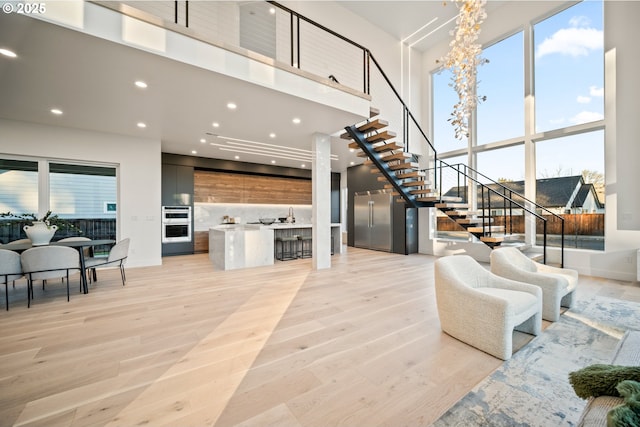 living area with stairs, light wood finished floors, plenty of natural light, and a towering ceiling