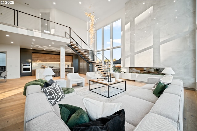 living room with a high ceiling, stairway, and light wood-type flooring