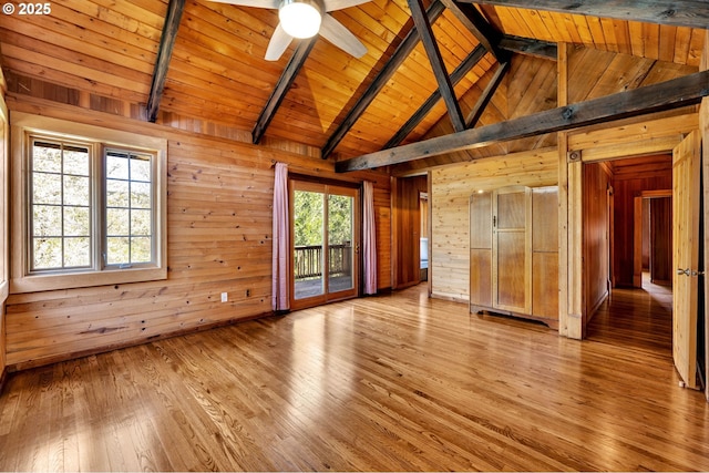 unfurnished living room with lofted ceiling with beams, a ceiling fan, wooden walls, and light wood-style flooring