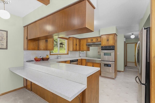 kitchen featuring a peninsula, brown cabinets, light countertops, baseboards, and appliances with stainless steel finishes