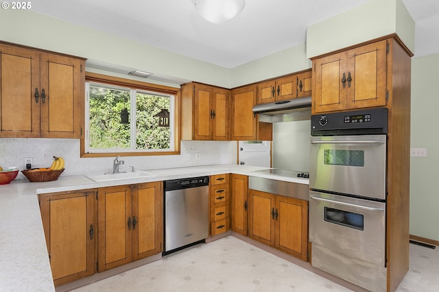 kitchen featuring a sink, brown cabinets, light floors, under cabinet range hood, and appliances with stainless steel finishes