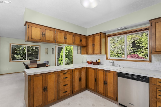 kitchen featuring a sink, stainless steel dishwasher, a peninsula, and brown cabinets