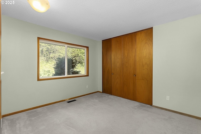 unfurnished bedroom with a closet, a textured ceiling, visible vents, carpet floors, and baseboards