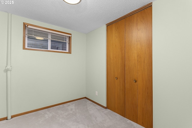 unfurnished bedroom featuring light colored carpet, a textured ceiling, a closet, and baseboards