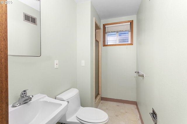 bathroom featuring toilet, a stall shower, a sink, visible vents, and baseboards