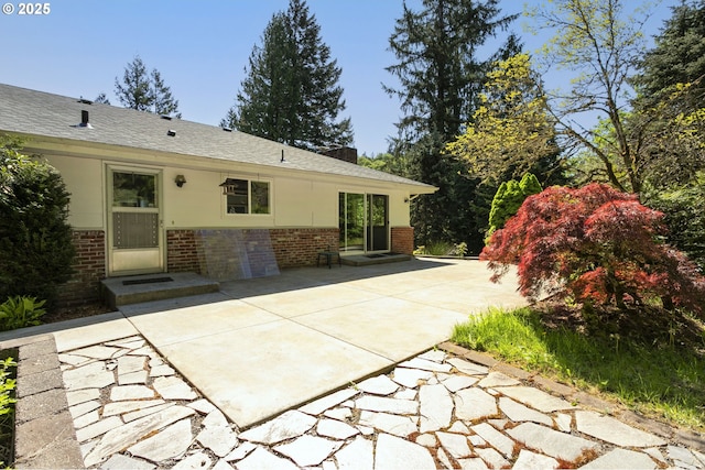 rear view of property with brick siding, roof with shingles, and a patio area