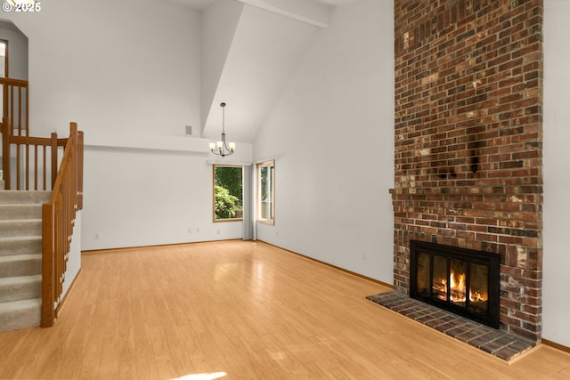 16149 SW Snapdragon Ln, Tigard, OR 97223 - unfurnished living room featuring wood finished floors, a brick fireplace, high vaulted ceiling, stairs, and a chandelier