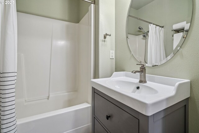 bathroom with shower / bathtub combination with curtain, a textured wall, and vanity