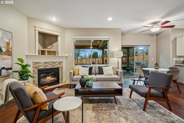 living room with baseboards, ceiling fan, wood finished floors, a stone fireplace, and recessed lighting