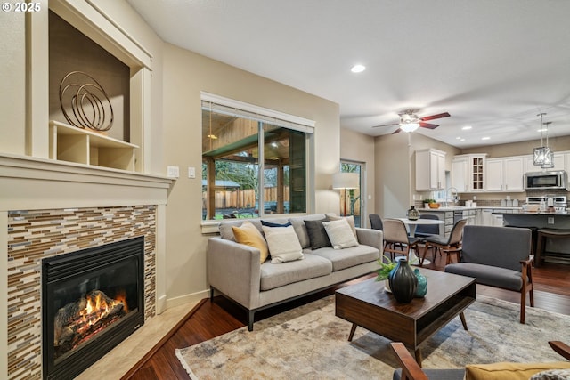 living room featuring baseboards, wood finished floors, a tile fireplace, and recessed lighting