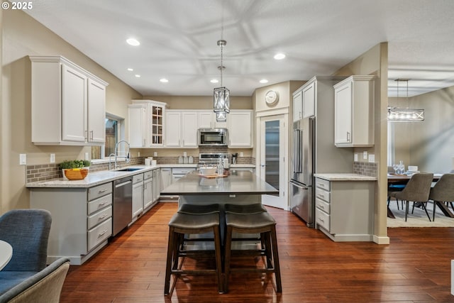 kitchen featuring a kitchen island, glass insert cabinets, decorative light fixtures, stainless steel appliances, and a sink