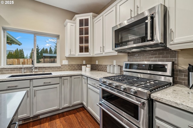 kitchen featuring white cabinets, dark wood finished floors, glass insert cabinets, light stone counters, and appliances with stainless steel finishes