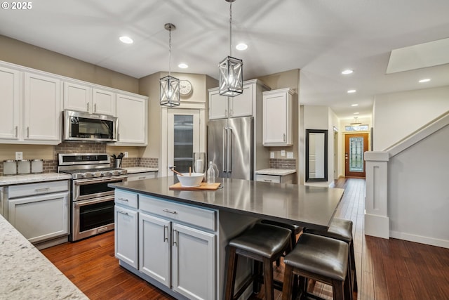 kitchen with pendant lighting, backsplash, appliances with stainless steel finishes, dark wood-type flooring, and white cabinets