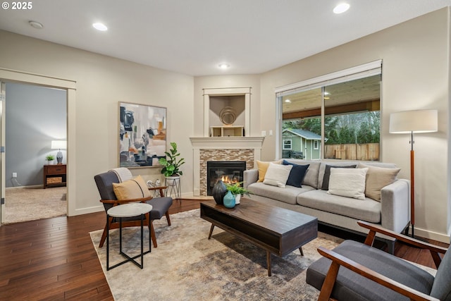 living room featuring recessed lighting, a stone fireplace, baseboards, and wood finished floors