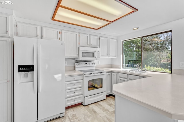 kitchen with light countertops, white cabinetry, a sink, white appliances, and a peninsula