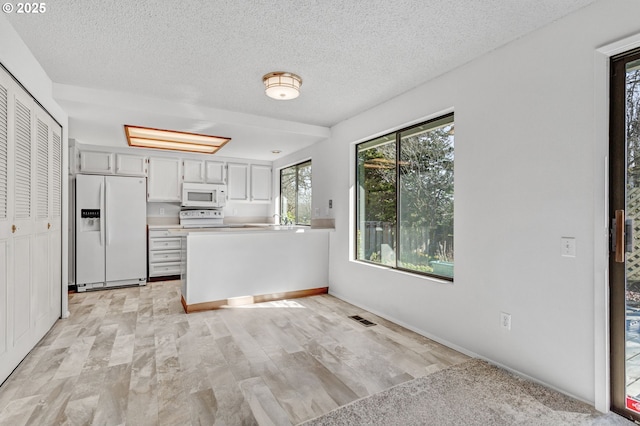 kitchen featuring a textured ceiling, a peninsula, white appliances, visible vents, and light countertops